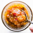 A spoonful of jalapeño mango chutney hovering above mason jar filled with chutney