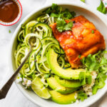 BBQ baked salmon fillet served in bowl with zucchini noodles and avocado slices.