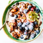 Grain free granola clusters in turquoise bowl with yogurt and fresh berries.
