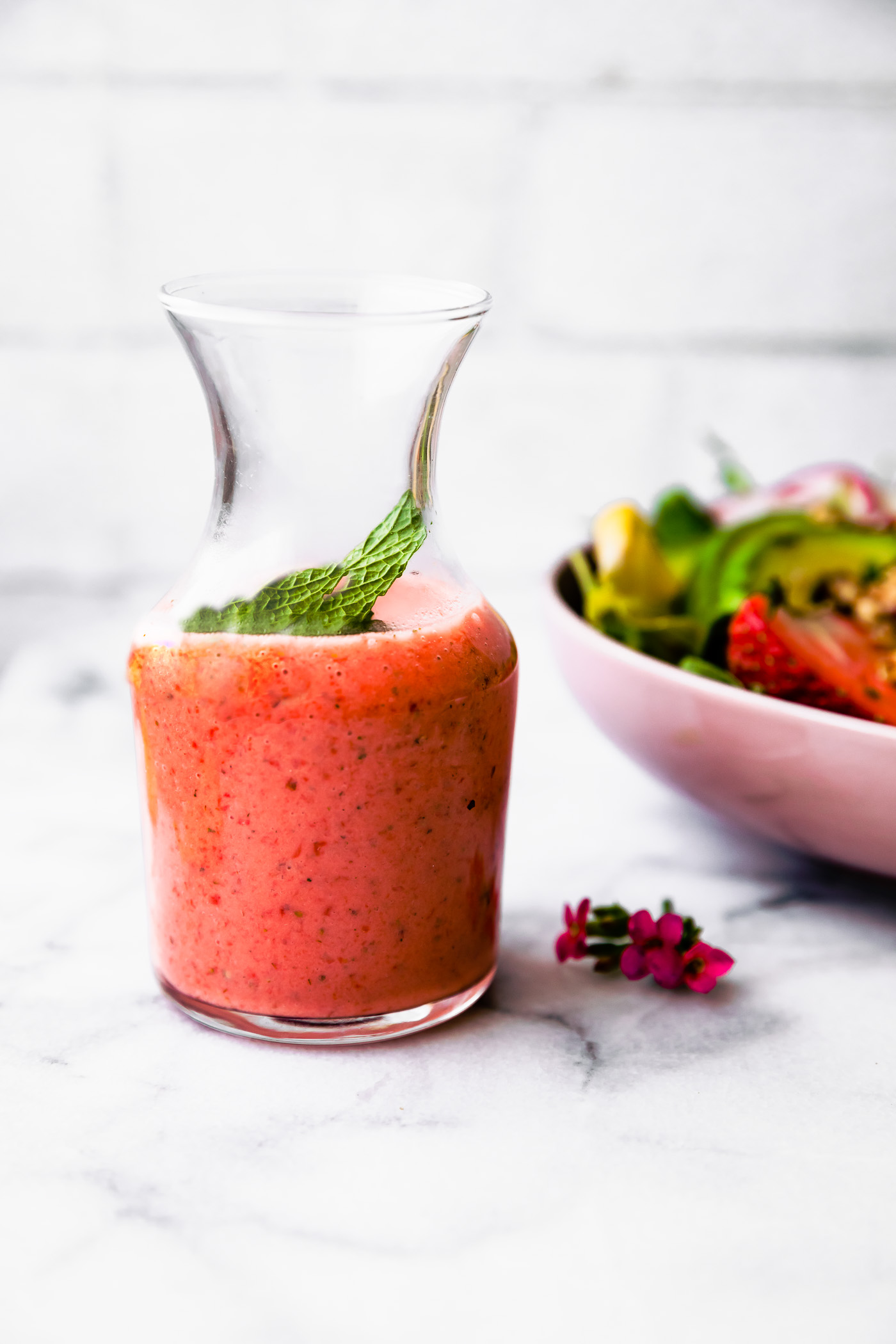 Strawberry vinaigrette dressing in clear glass carafe with mint leaf on top.