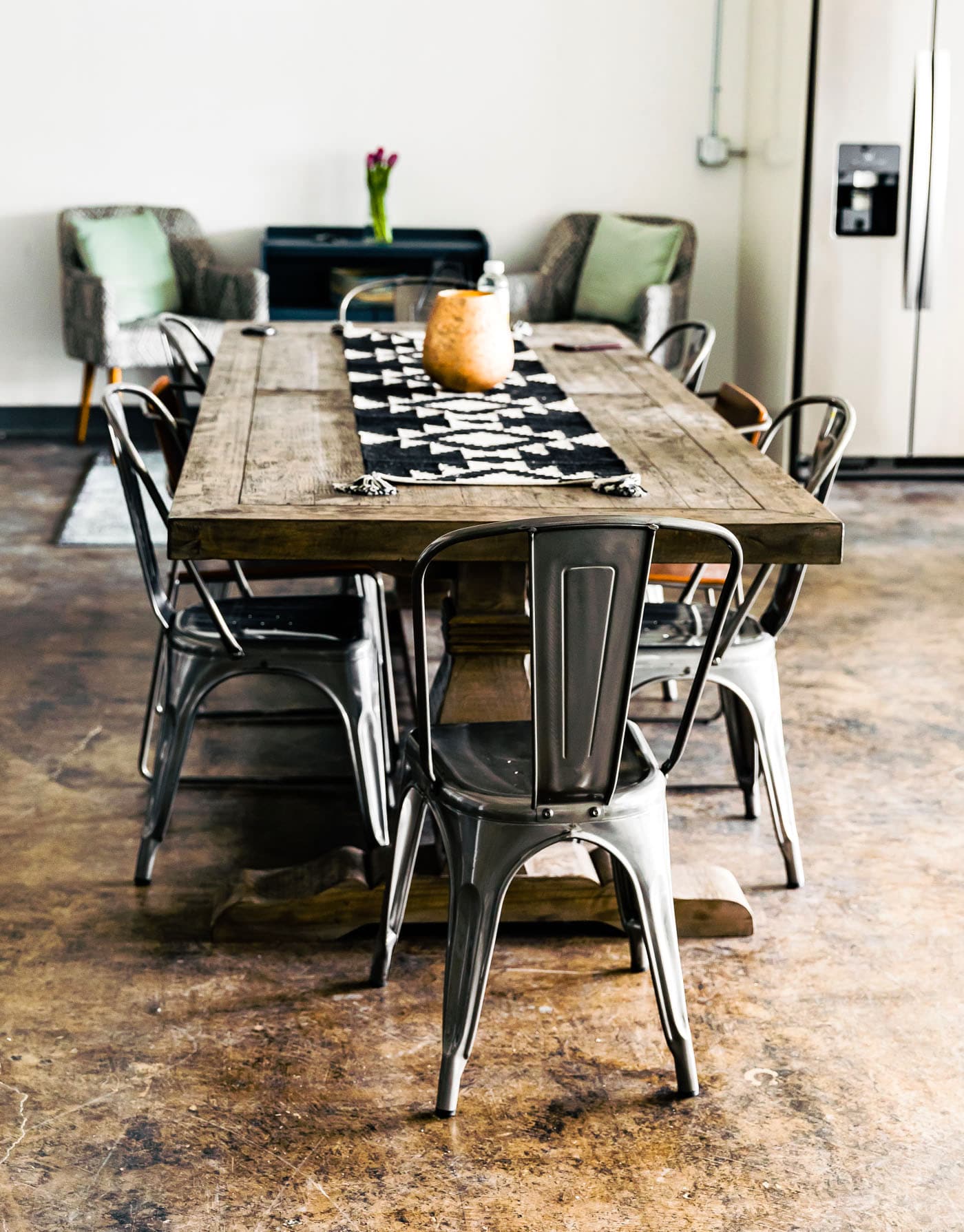 Long wooden table with metal chairs, table runner in black and white.