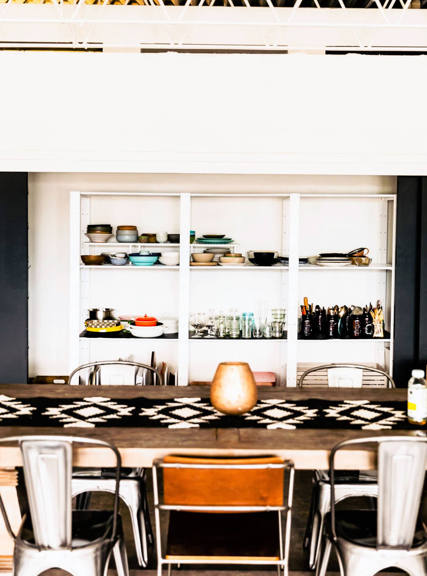 A beautiful kitchen table with metal chairs with built in shelves behind filled with food photography props