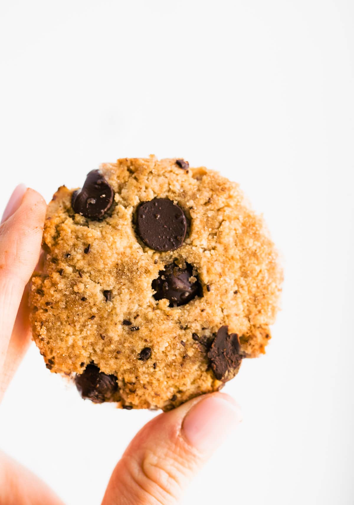 An almond flour chocolate chip cookie being held between two fingers.
