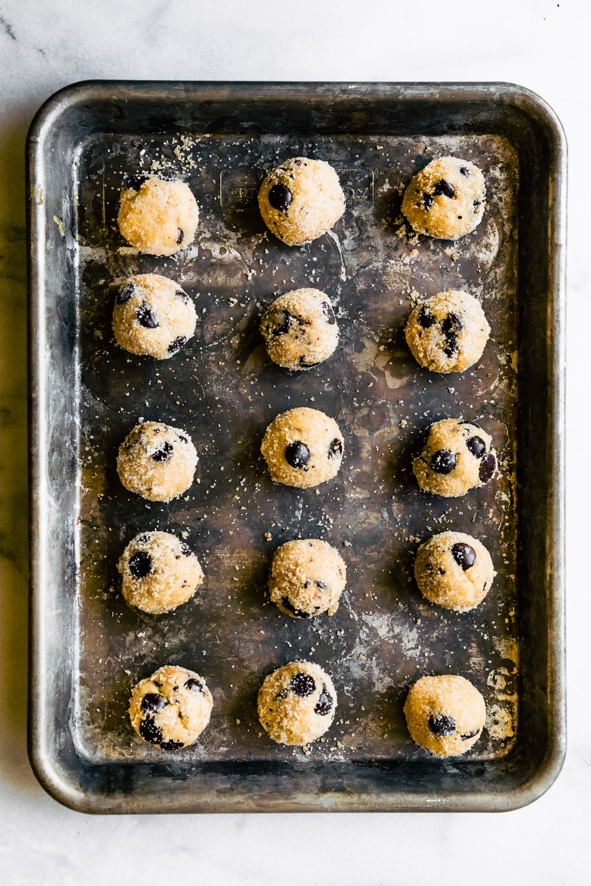 Almond flour chocolate chip cookie dough balls lined up on deep baking sheet.