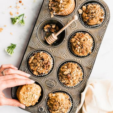Overhead view eight-count muffin tin filled with breakfast muffins topped with granola, one muffin being removed from pan.
