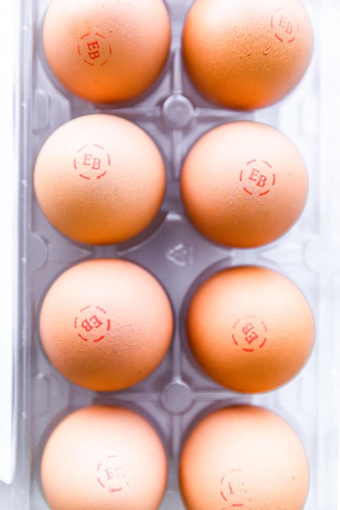 Overhead view brown eggs stamped with letters 'EB', in carton.