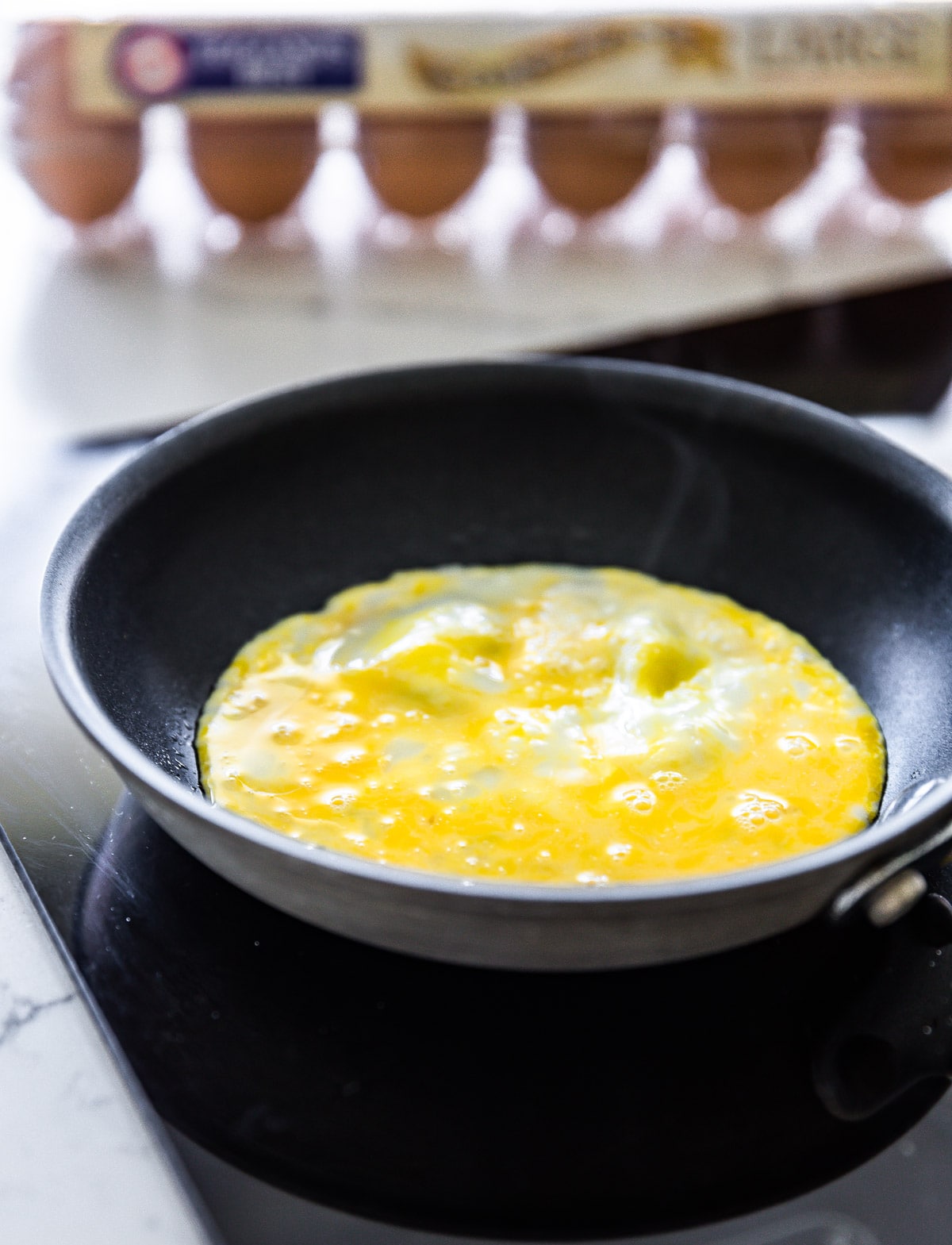 Whipped eggs cooking in small black skillet for egg wrap recipe