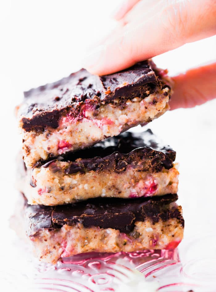 stack of no bake protein bars topped with chocolate, one bar being picked up from top of stack