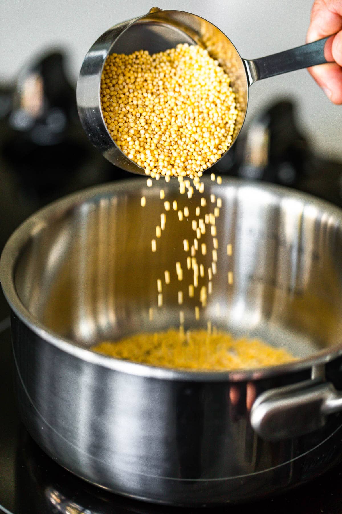 A measuring cup filled with millet being poured into saucepan