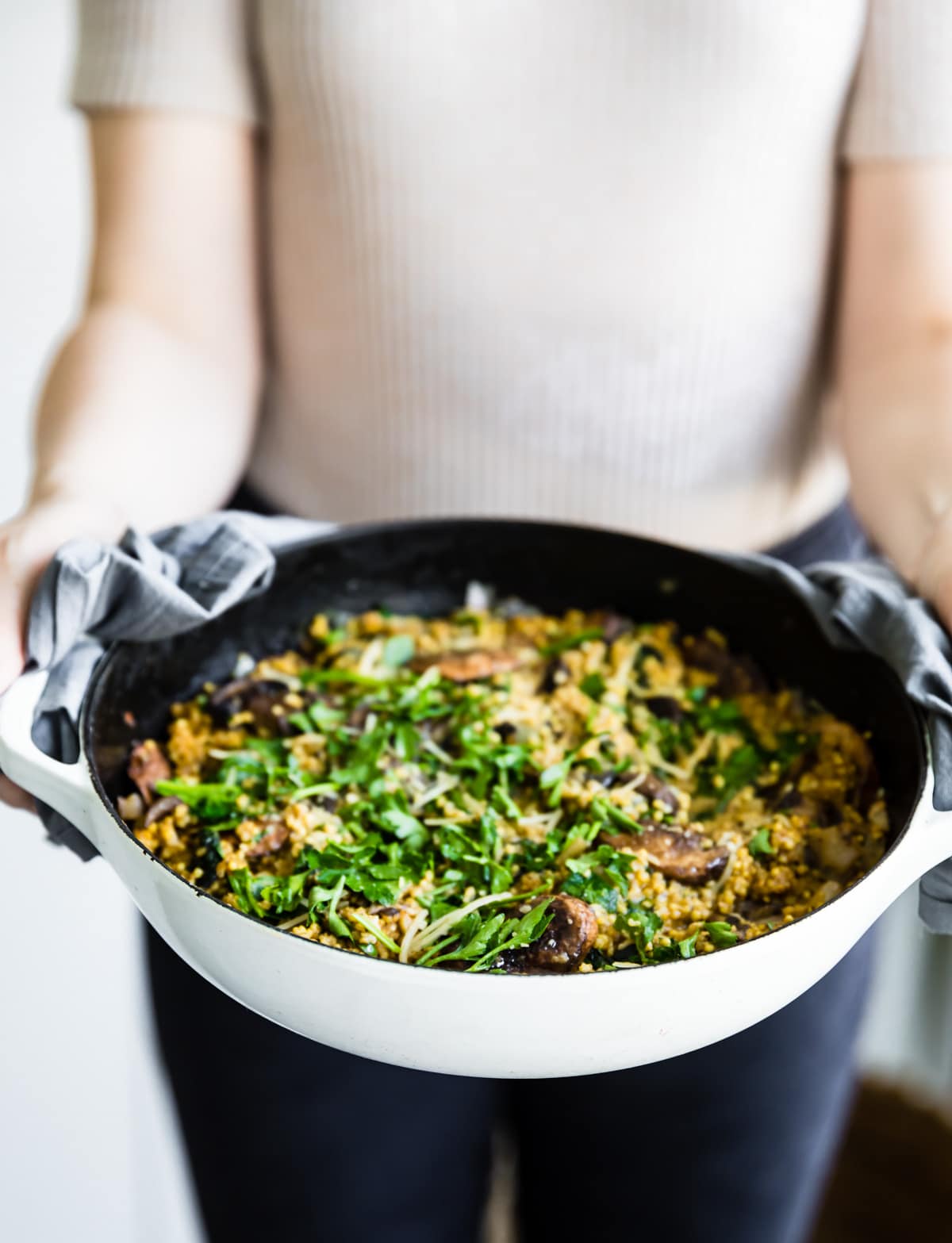 A woman holding pan of mushroom risotto with millet, topped with greens