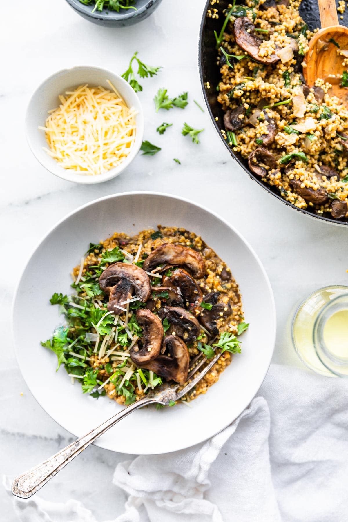 Overhead view creamy mushroom risotto with millet in white bowl topped with mushrooms and fresh greens