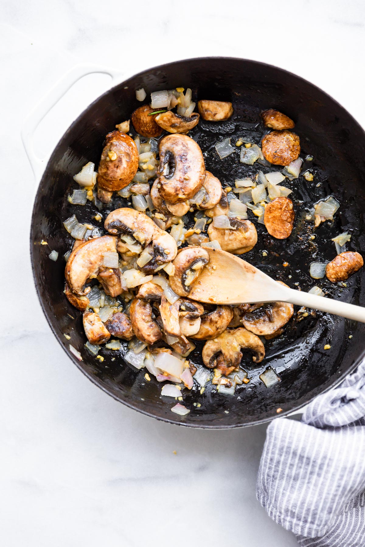 overhead view sautéed mushrooms and onions in skillet with wooden spoon