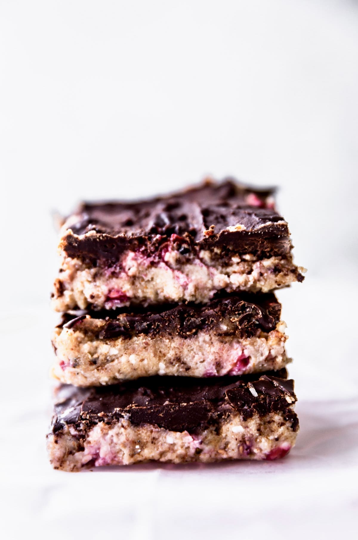 Stack of no bake chocolate almond protein bars with dried fruit, topped with chocolate
