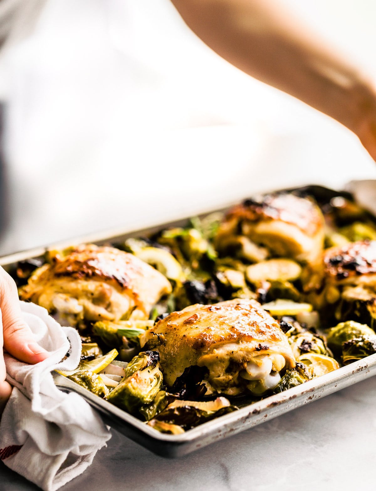 Two hands holding baking sheet filled with roasted honey mustard chicken thighs and roasted Brussels sprouts