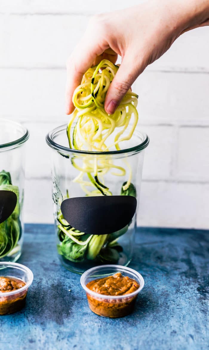 A hand adding zucchini zoodles into a Weck jar with a black label.