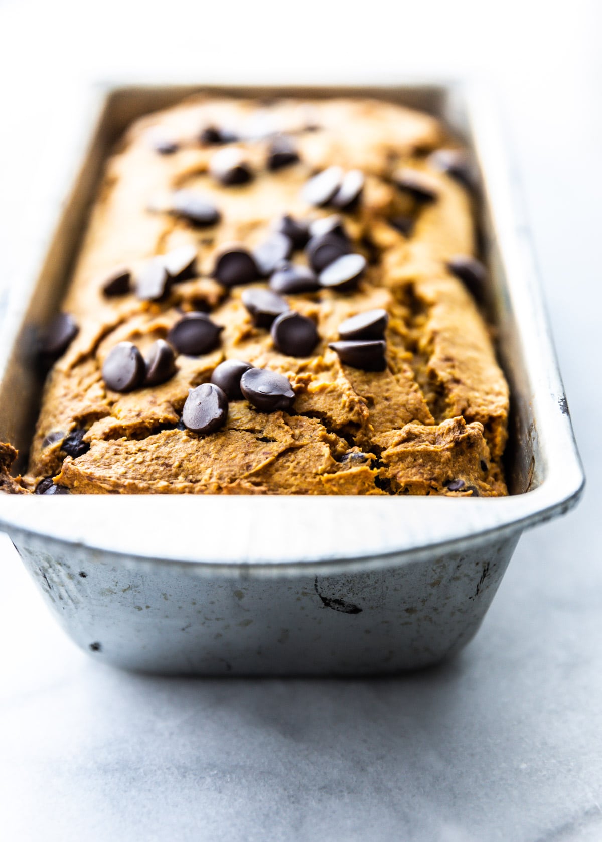 Straight on view vegan pumpkin bread topped with dark chocolate chips in silver bread pan