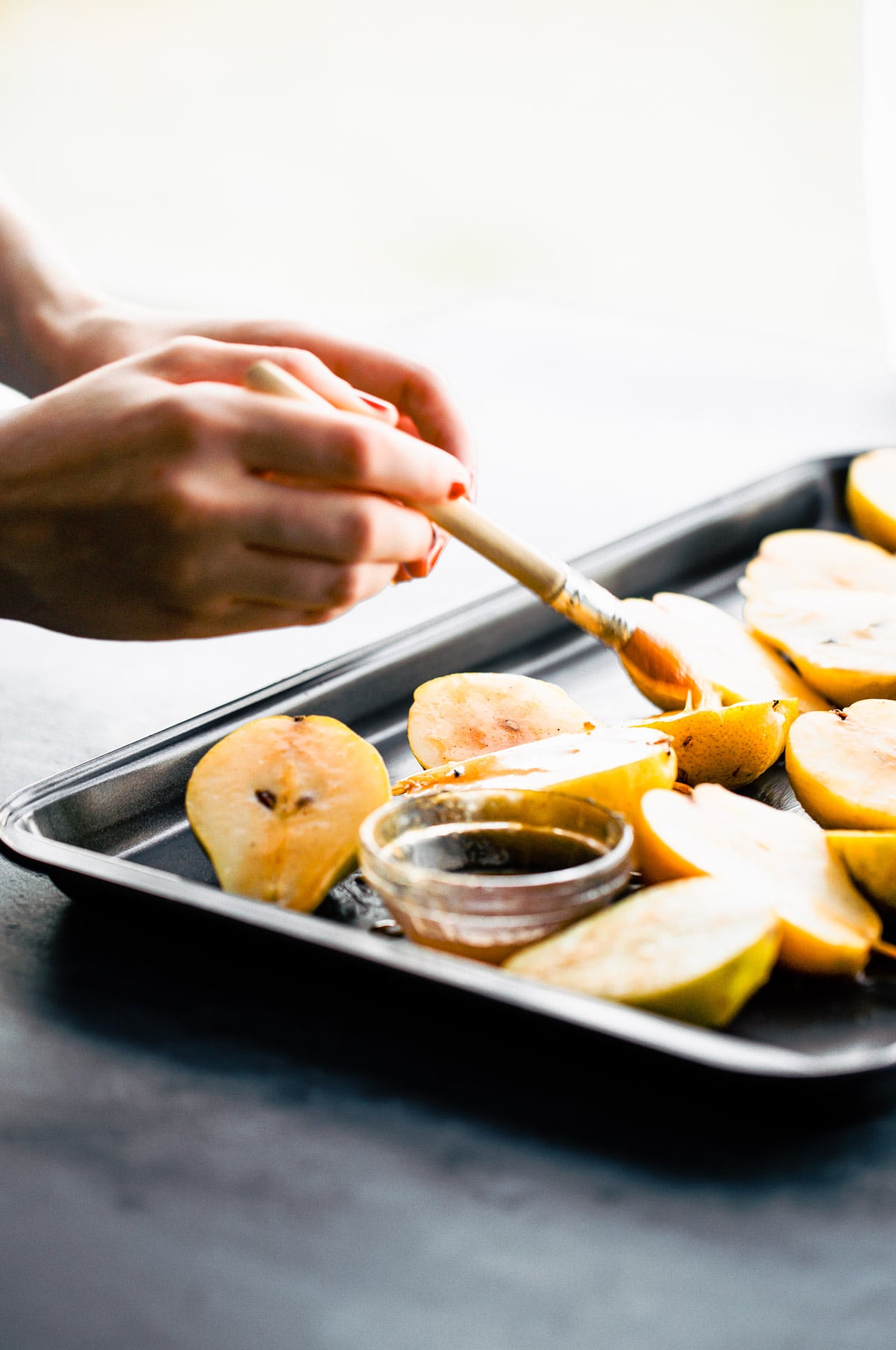 A hand brushing glaze on pear halves on baking sheet for. baked pears.