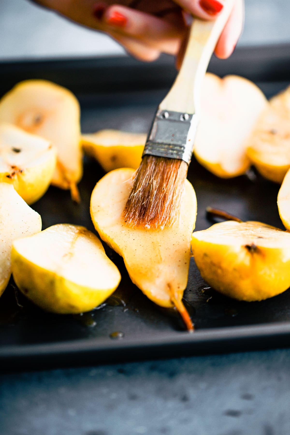 Maple glaze being brushed onto pear halves on baking sheet.
