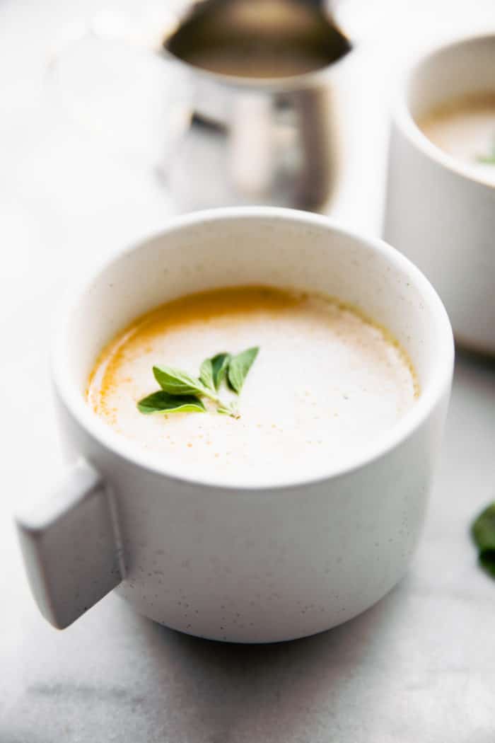 warm bone broth latte in white coffee mug topped with sprig of fresh herbs