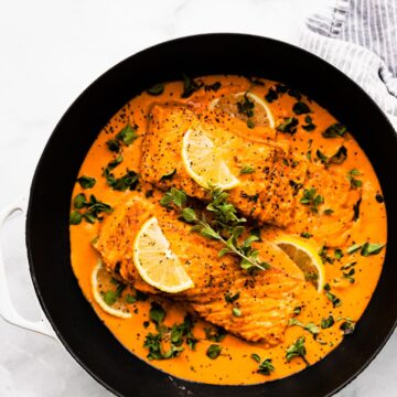Overhead view baked salmon in roasted red pepper sauce in white and black skillet