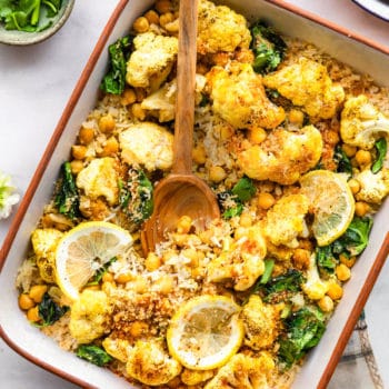 Curried Cauliflower Chickpea Bake in white baking dish with wooden spoon in dish.