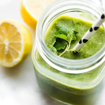Bright green smoothie in mason jar cup topped with fresh mint