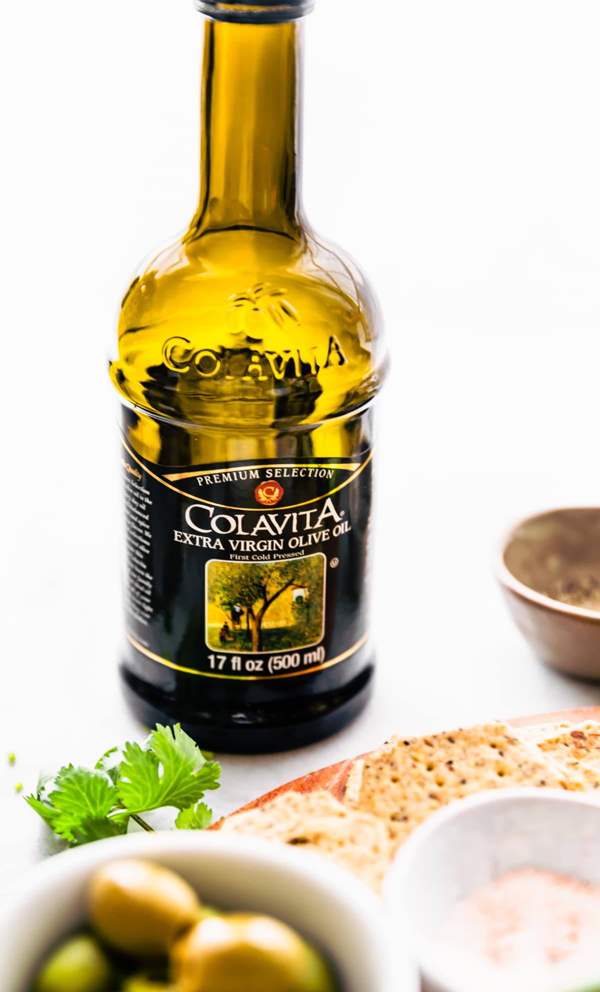 bottle of Colavita extra virgin olive oil with tray of snacks in front 