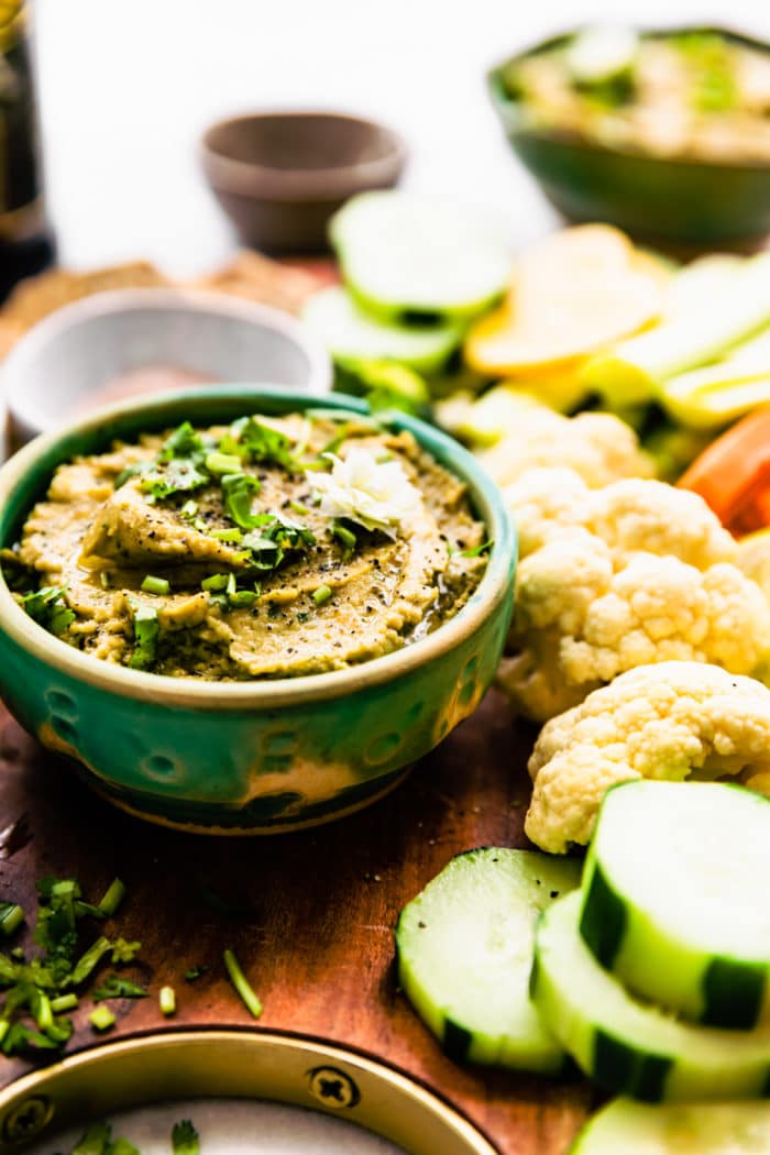 hummus dip in small green bowl surrounded by fresh veggies for dipping
