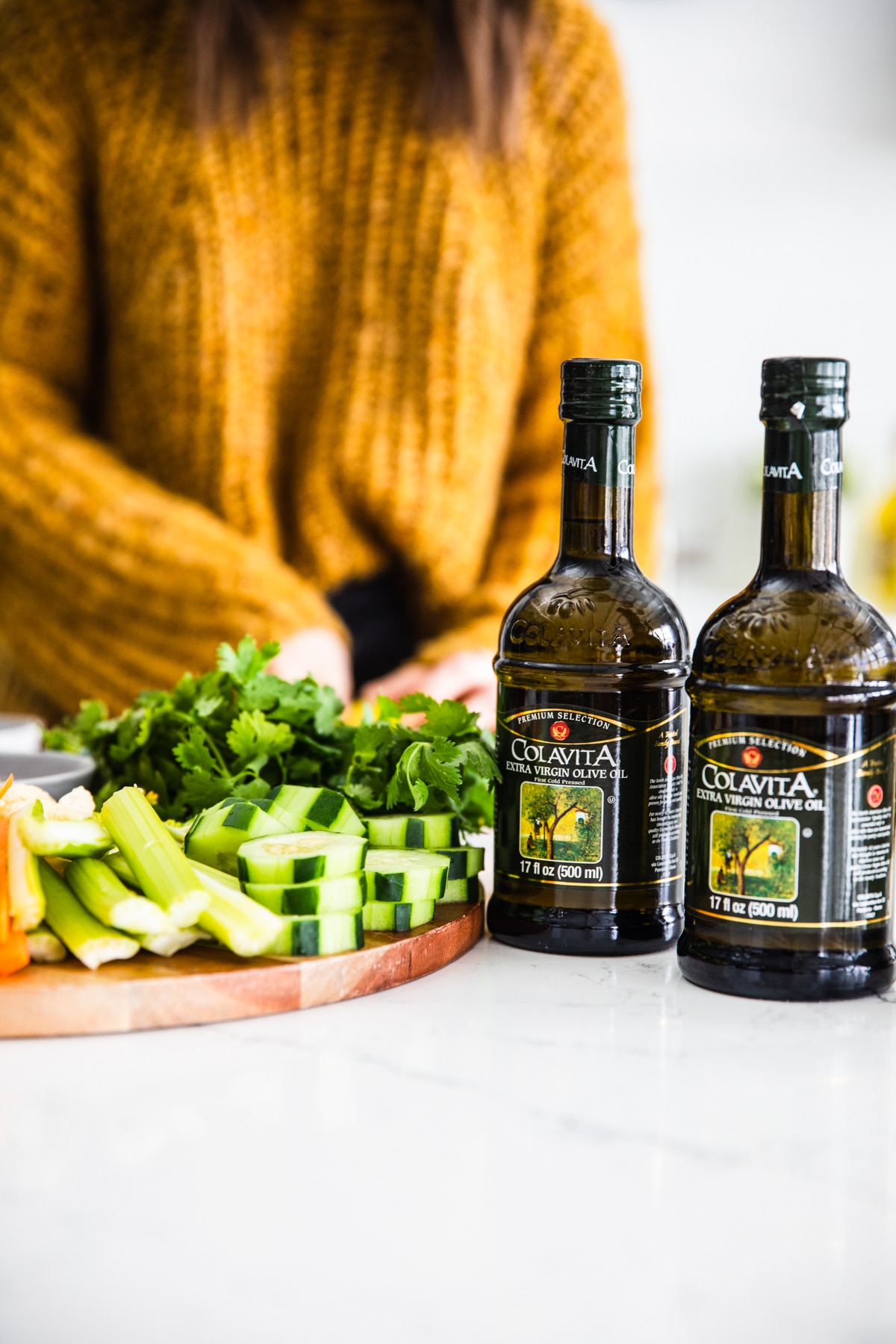 2 dark glass bottles of olive oil on counter next to wooden cutting board filled with fresh cut vegetables.