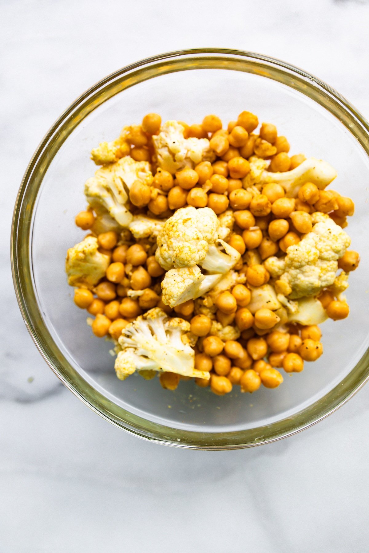 Overhead photo of a clear glass bowl filled with curried cauliflower florets and chickpeas.