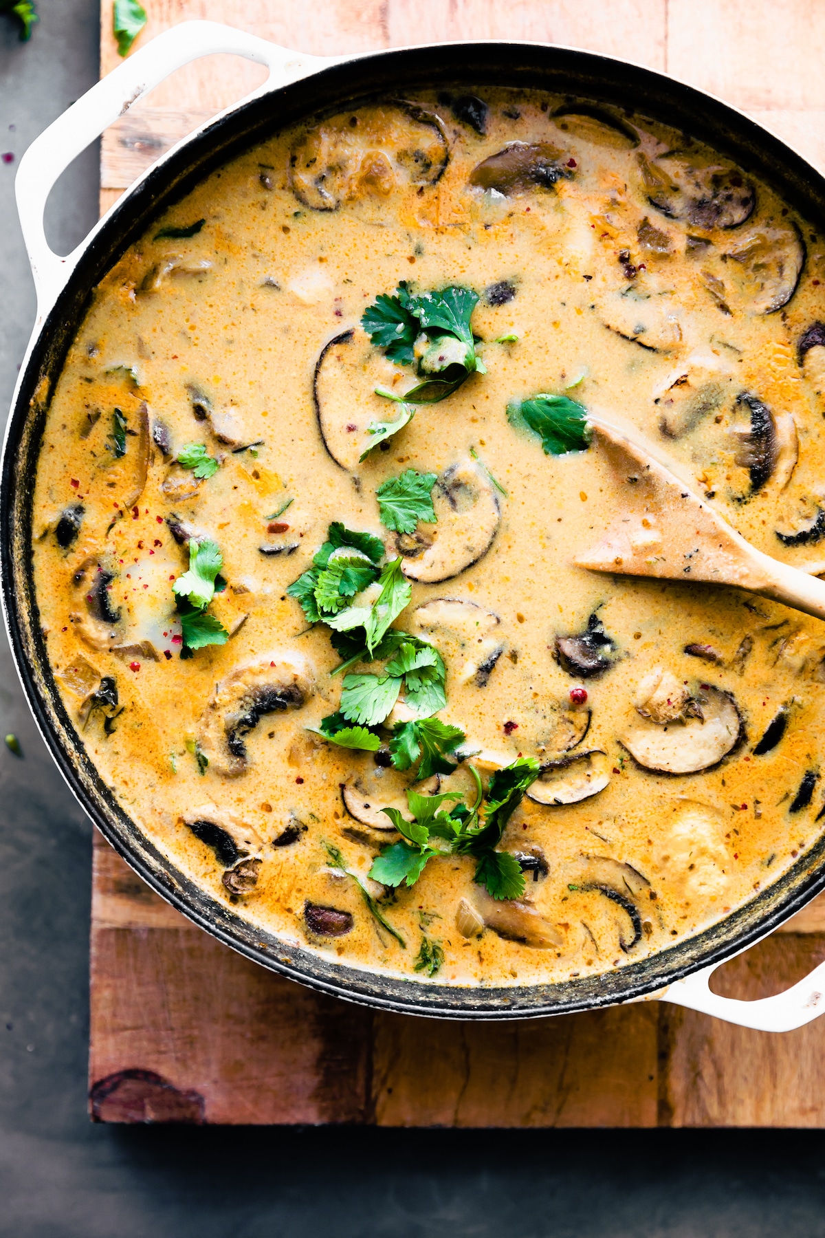 creamy vegan mushroom soup in a pot topped with fresh herbs being stirred with a wooden spoon