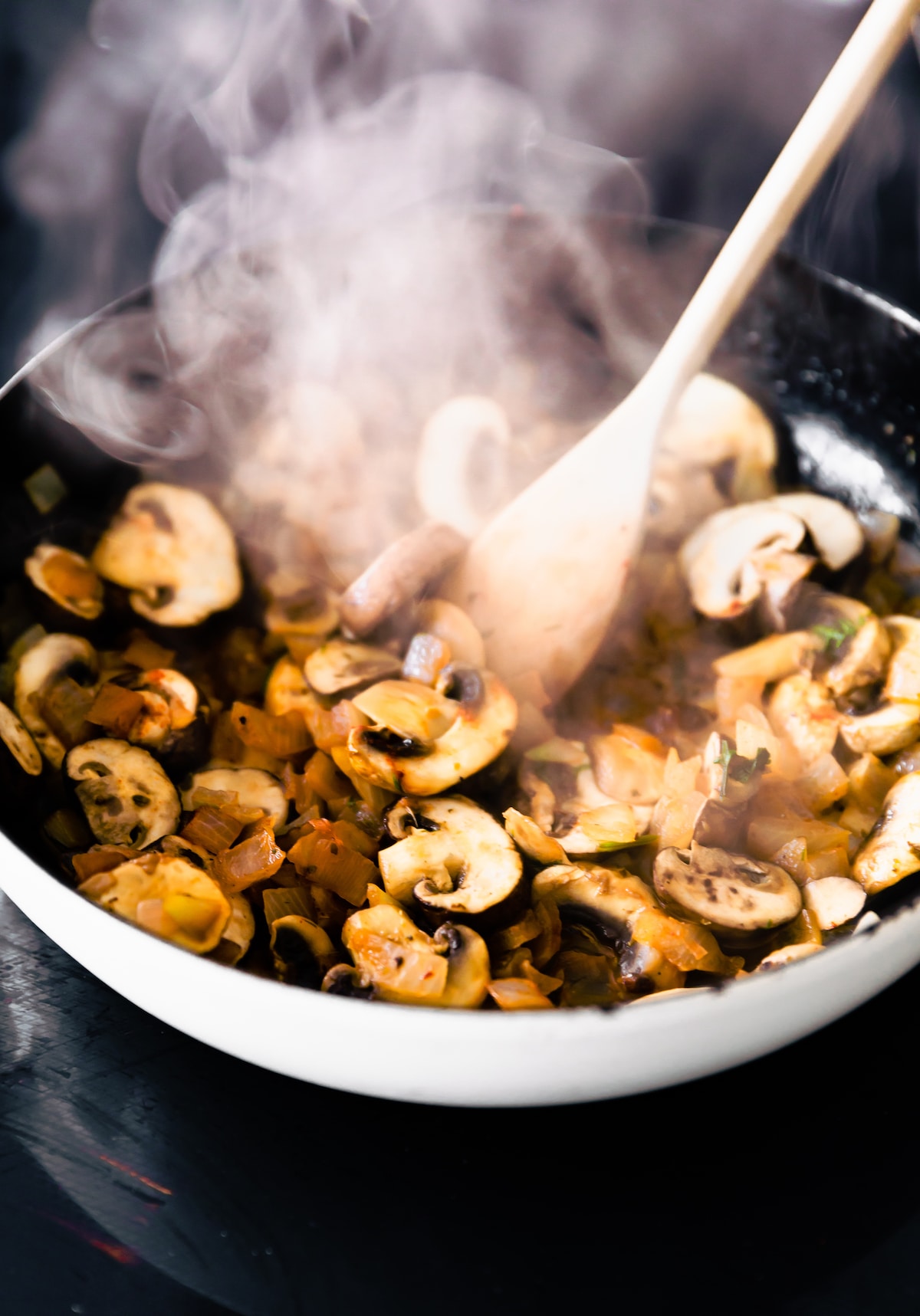 mushrooms sweating in a skillet being stirred with a wooden spoon