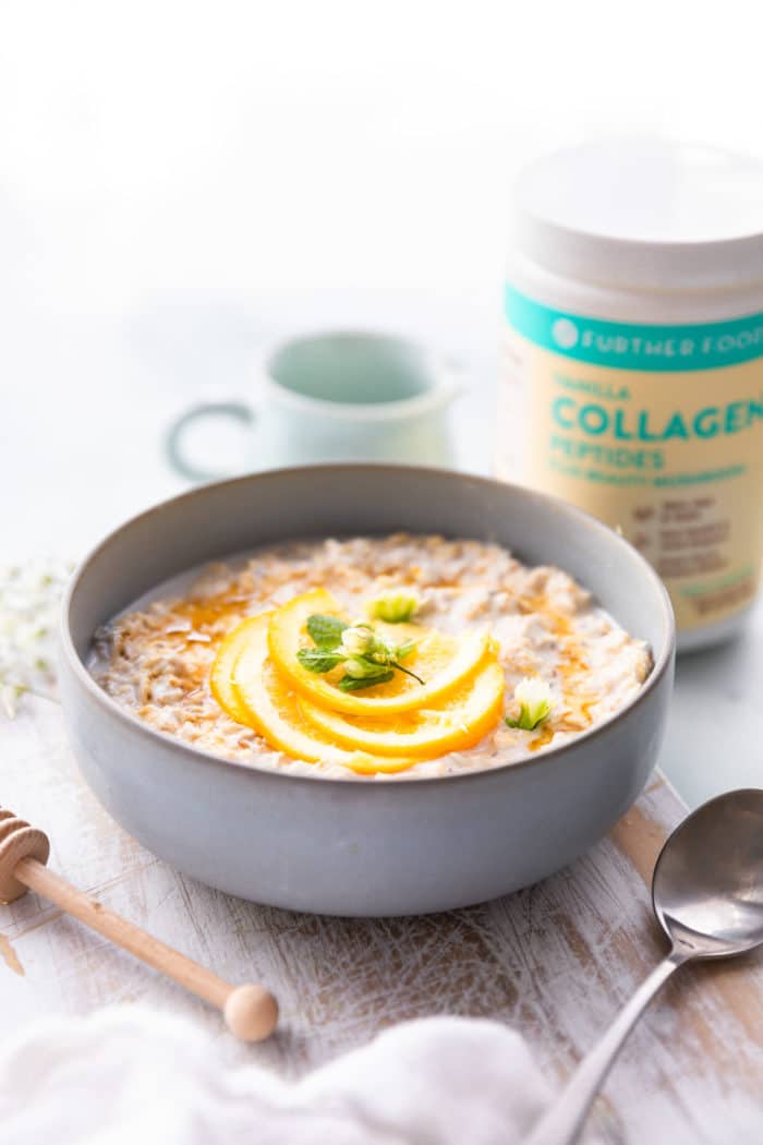 bowl of oatmeal with orange slices. Jar of collagen in the background