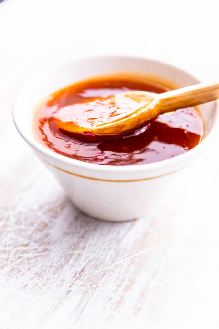 homemade sweet and sour sauce in white bowl with small wooden spoon.