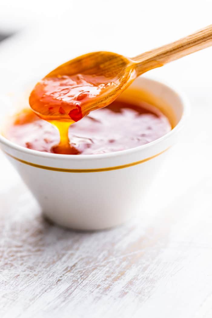 homemade sweet and sour sauce in white bowl and on wooden spoon
