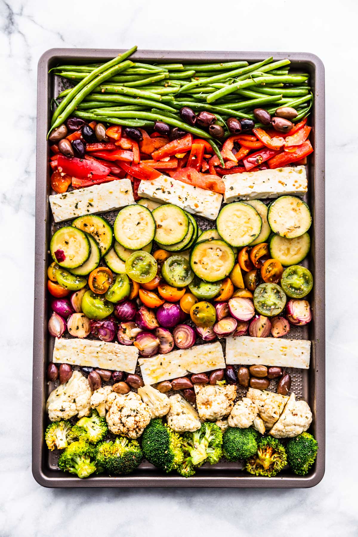 Baking sheet filled with Greek seasoned fresh veggies and feta ready for the oven.