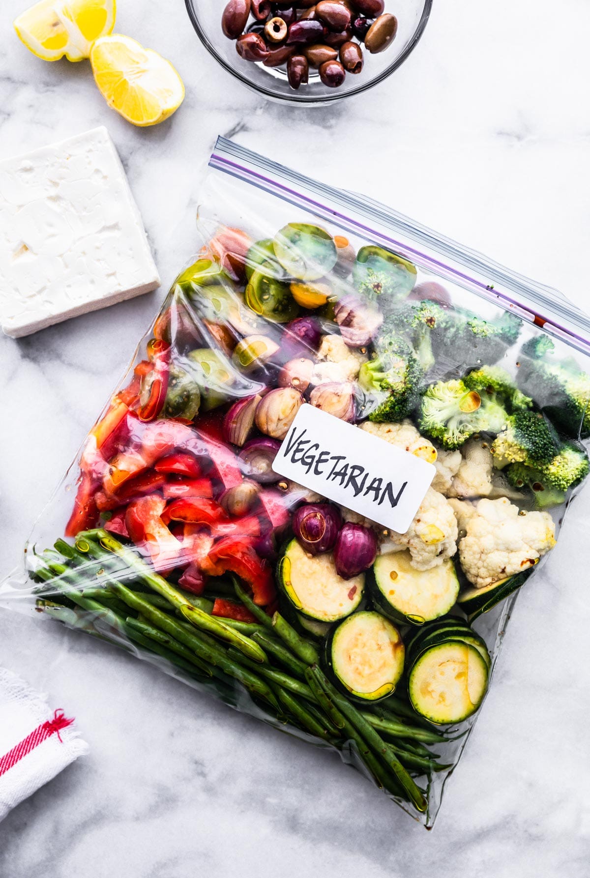 Ziplock bag filled with fresh veggies with Greek seasonings on marble countertop