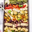 Two hands holding sheet pan filled with Greek vegetables and feta