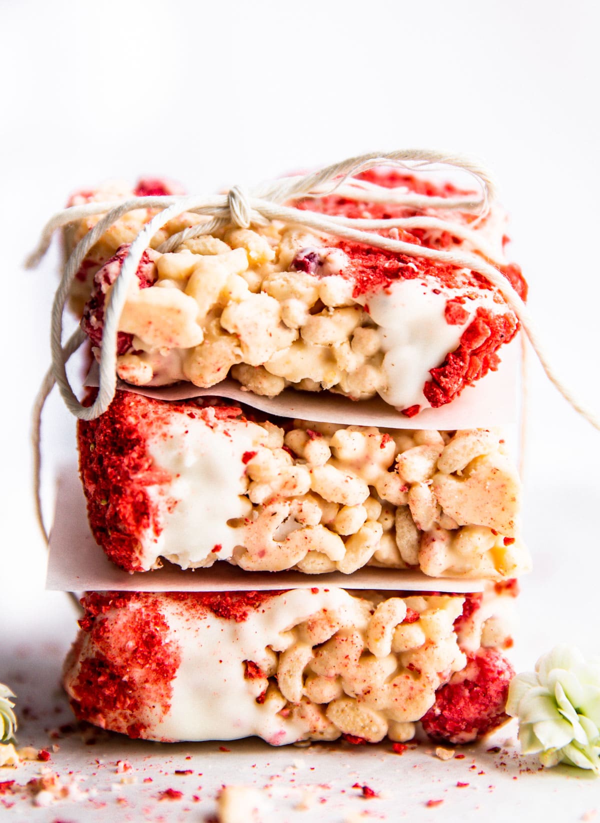 Three white chocolate raspberry rice crispy treat bars stacked up on each together tied together with a piece of twine.