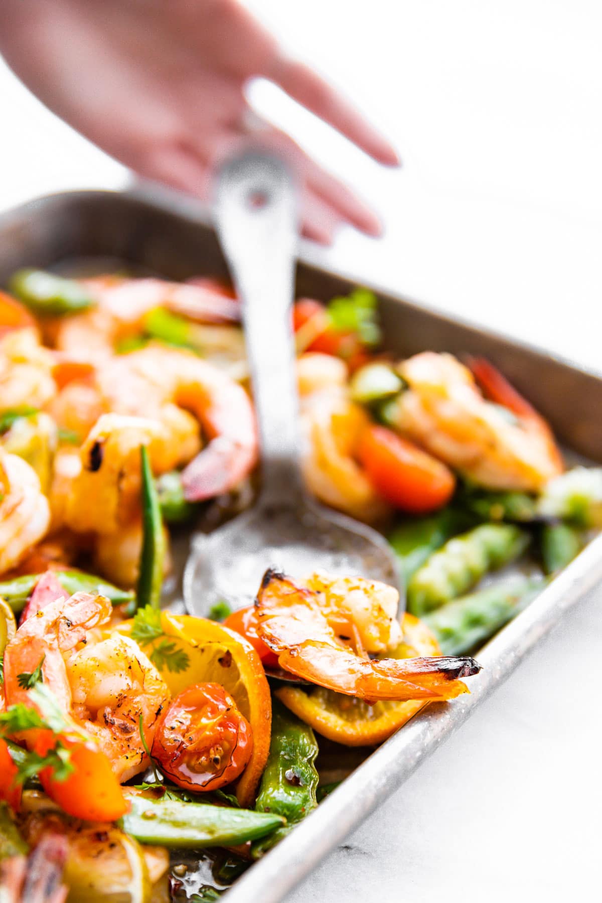 Close up side view broiled shrimp and vegetables on sheet pan with large serving spoon.