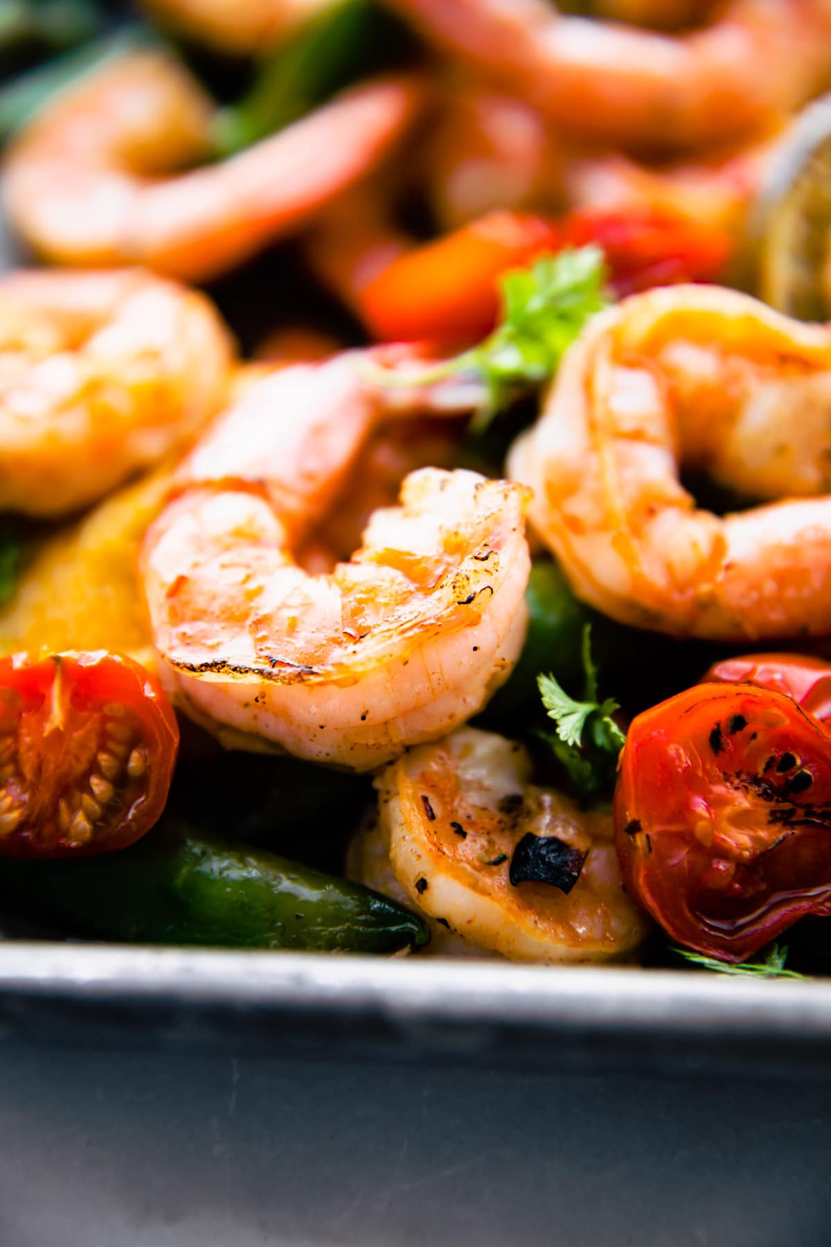 Close up view sweet and spicy broiled shrimp with roasted vegetables on sheet pan.