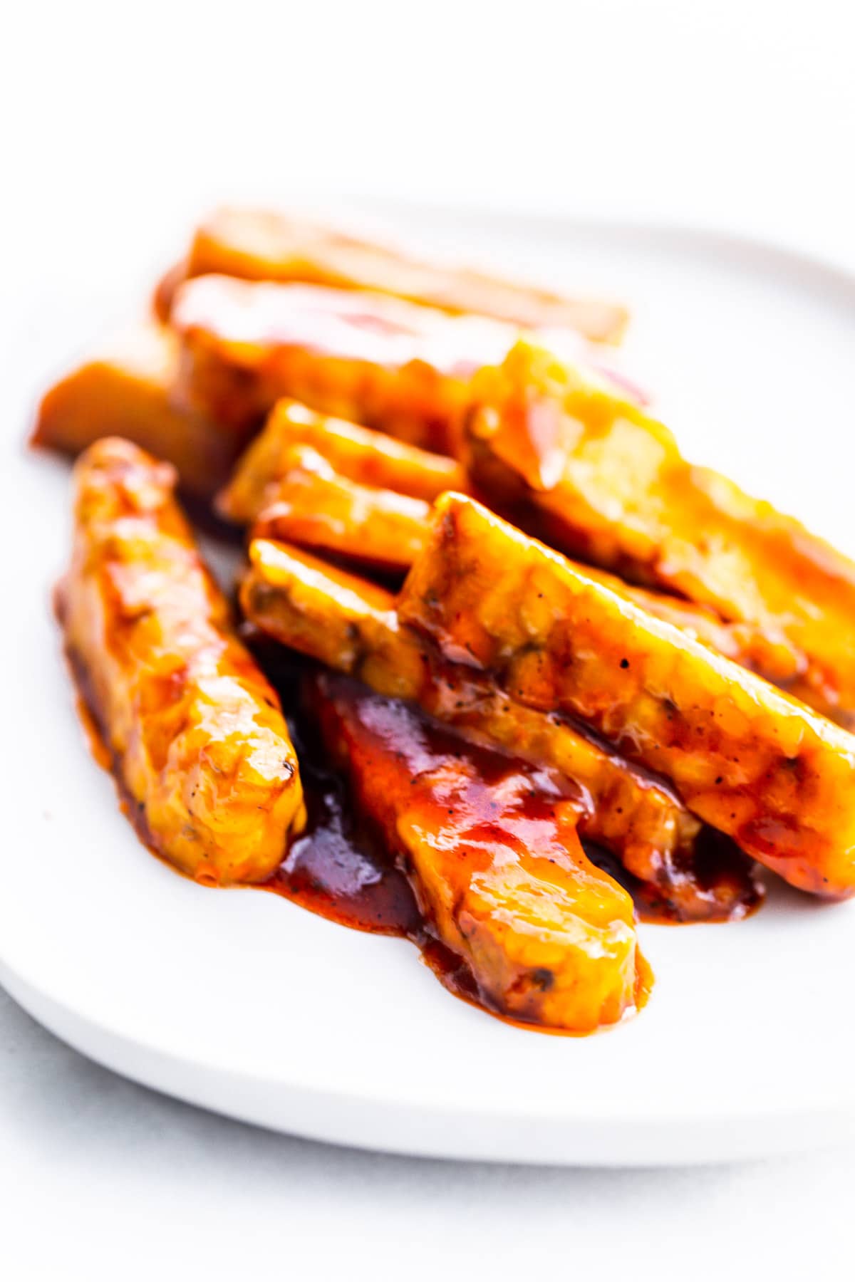 A pile of bbq tempeh strips on white plate.
