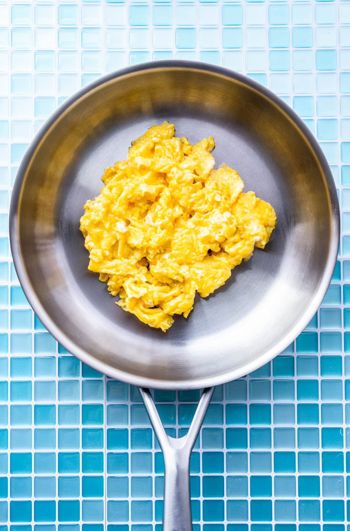 Overhead view of scrambled eggs in a silver skillet.