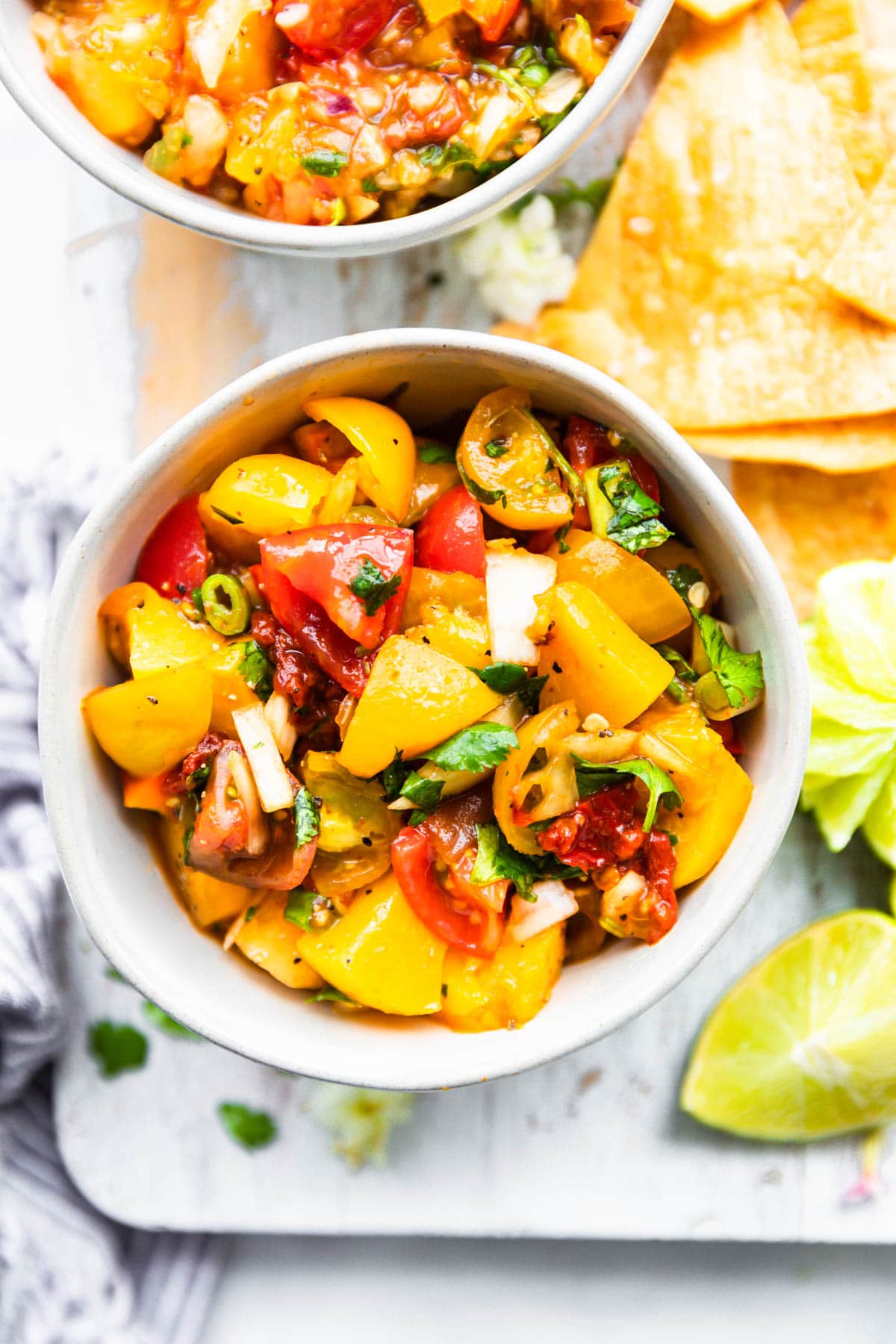 homemade chipotle peach salsa in bowl on wooden cutting board surrounded by tortilla chips.