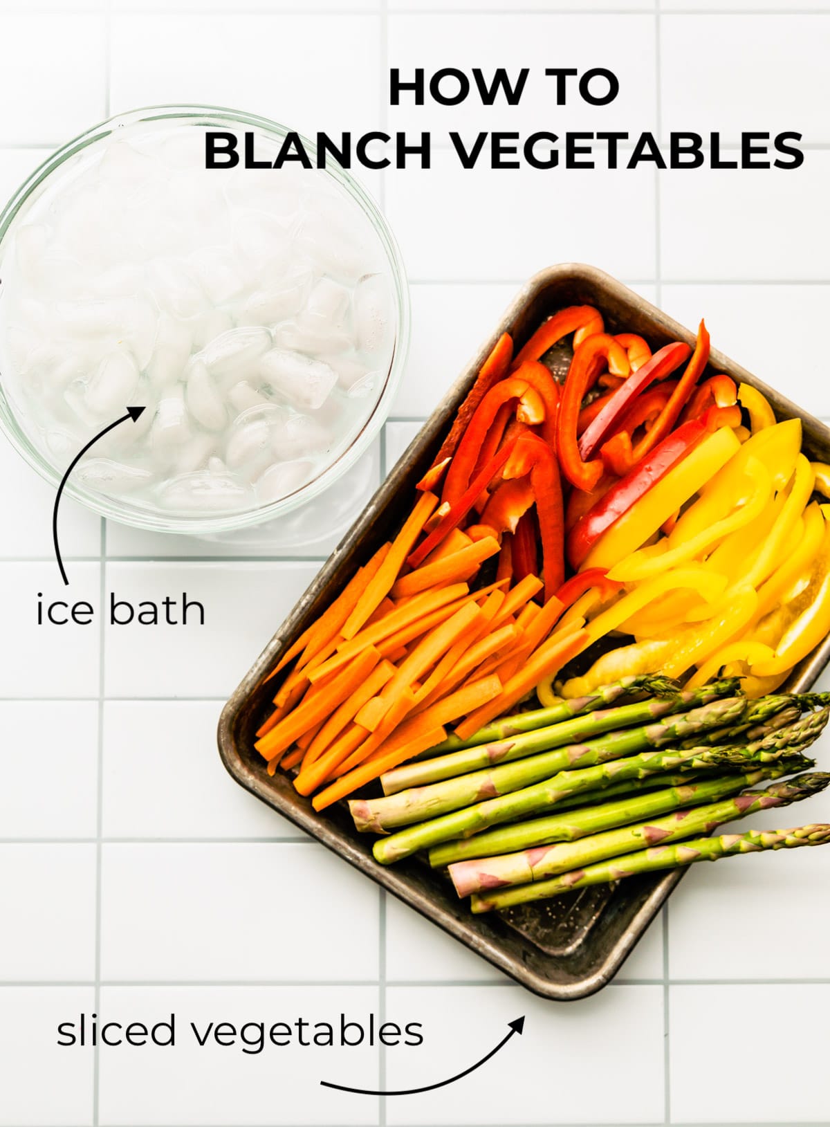 Baking sheet filled with cut carrots, peppers in red and yellow, and cut asparagus. Bowl of ice water next to baking sheet.
