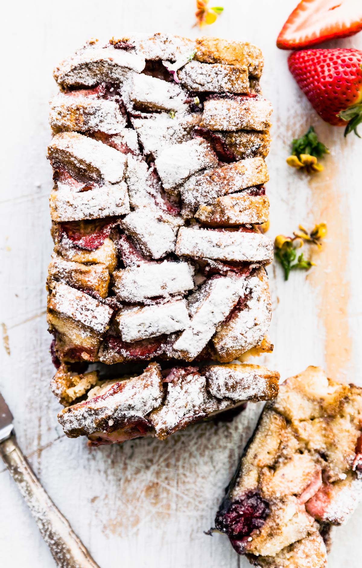 loaf of french toast pull apart bread with strawberries, placed on white wooden cutting board