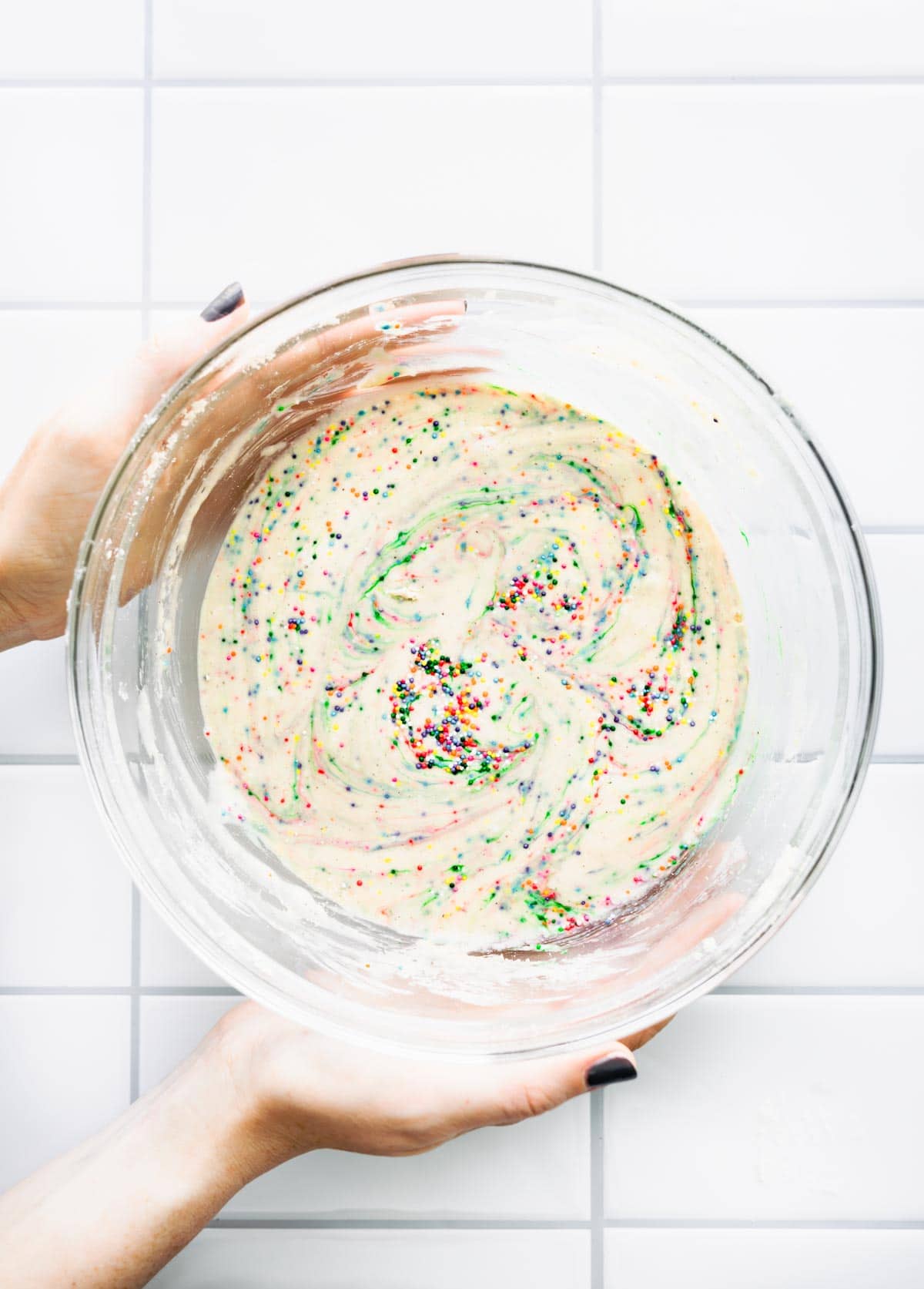 woman's hands holding glass mixing bowl full of batter with colored sprinkles