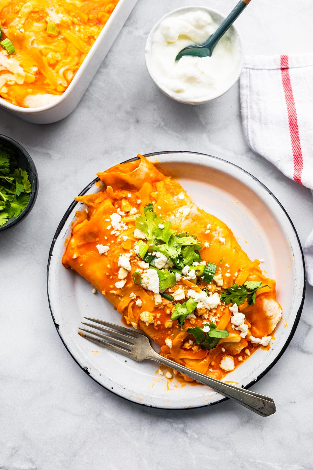buffalo style enchiladas on plate topped with fresh cilantro with fork on the side.
