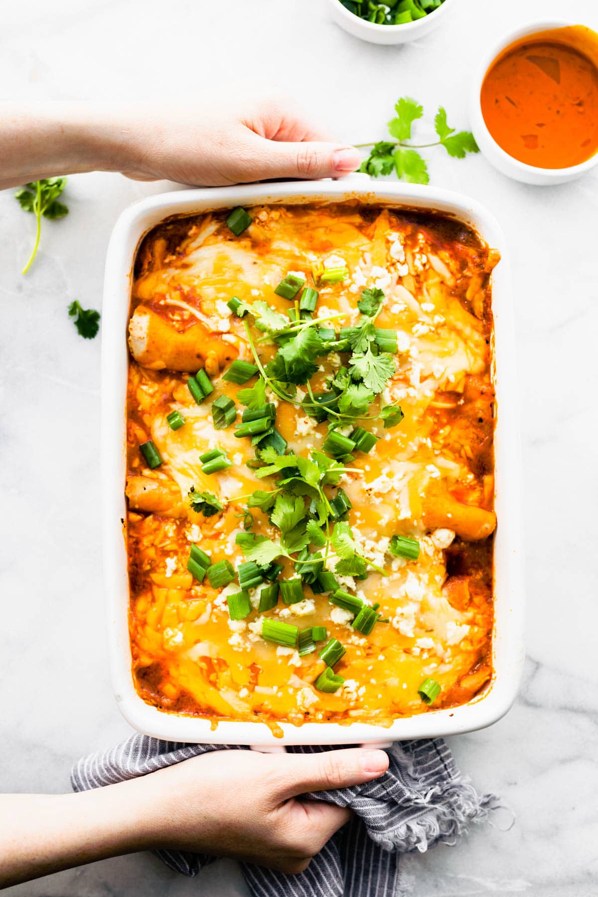 Two hands holding white baking dish filled with easy enchiladas casserole