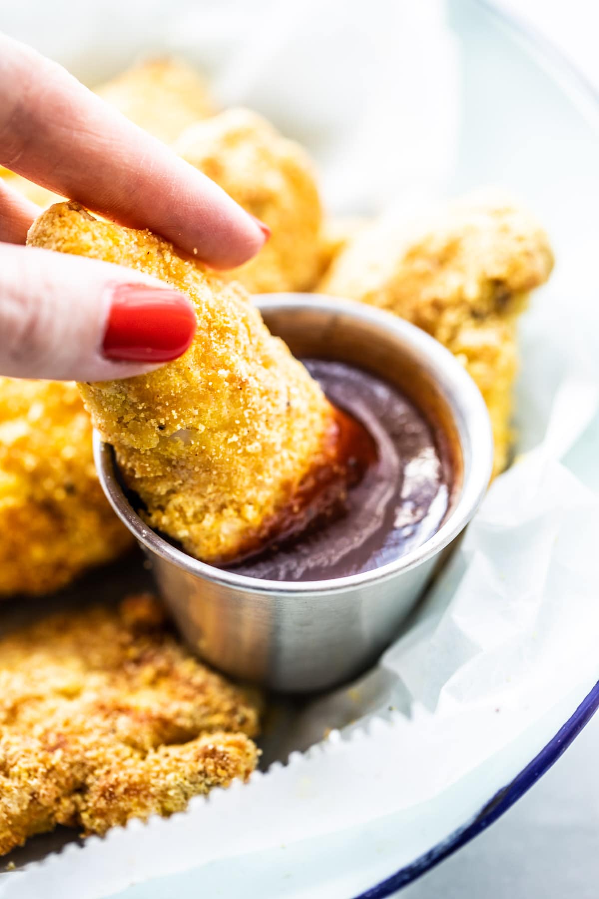 woman's fingers holding air fryer chicken tenders, dipping it into bbq sauce